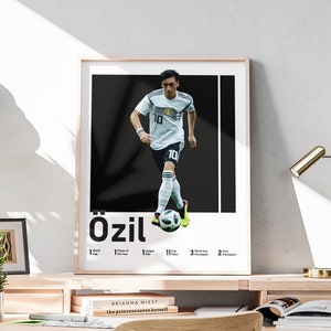 May include: A black and white poster featuring a soccer player in a white jersey with the number 10 on it. The player is dribbling a soccer ball. The poster has the text "Özil" in large, bold letters and a list of his accomplishments.