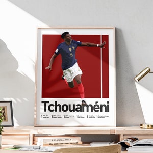 Könnte beinhalten: Ein rotes und weißes Poster mit einem Foto eines Fußballspielers in einem blau-weißen Trikot. Der Spieler ist in der Luft und tritt einen Fußball. Das Poster trägt den Text "Tchouaméni" in schwarzen Buchstaben. Das Poster listet auch die Leistungen des Spielers auf, darunter "1 FIFA Club World Cup Sieger", "1 UEFA Nations League Sieger", "1 UEFA Supercup Sieger", "1 spanischer Pokalsieger", "1 Vize-Weltmeister", "1 Champions League Teilnehmer".