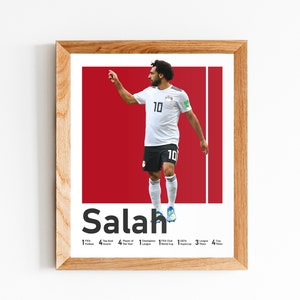 K&ouml;nnte beinhalten: Ein gerahmtes Poster mit einem Foto von Mohamed Salah, einem professionellen Fu&szlig;ballspieler, in einem wei&szlig;en Trikot mit der Nummer 10. Das Poster hat einen roten Hintergrund und den Text "Salah" in fetten schwarzen Buchstaben. Das Poster enth&auml;lt auch eine Liste von Salahs Leistungen, darunter "1 FIFA Puskas Award", "4 Premier League Titel", "4 Spieler des Jahres Auszeichnungen", "1 Champions League Titel", "1 FIFA Club World Cup", "3 UEFA Supercup", "3 League Cup Titel" und "4 FA Cup Titel".