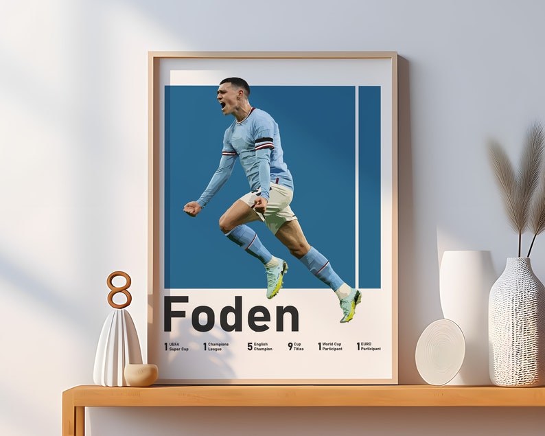 May include: A poster featuring a football player in mid-air, celebrating a goal. The player is wearing a light blue jersey with white accents and black shorts. The poster has a blue background with a white vertical line. The player's name, "Foden", is written in large white letters below the image. The poster also lists the player's accomplishments, including 1 UEFA Super Cup, 1 Champions League, 5 English Champions, 9 Premier League Titles, 1 World Cup Participant, and 1 EURO Participant.