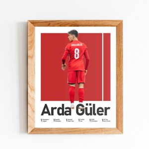 May include: A framed poster featuring a soccer player wearing a red jersey with the number 8 on the back. The player's name, "Arda G&uuml;ler", is printed in bold white letters below the image. The poster also lists the player's accomplishments, including "1x Turkish Cup", "1x Turkish Super Cup", and "1x Turkish League Champion".