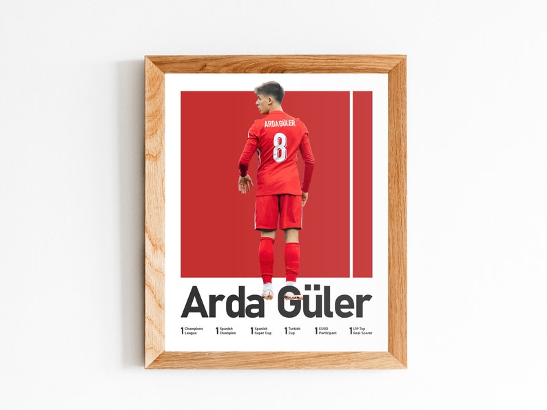 May include: A framed poster featuring a soccer player wearing a red jersey with the number 8 on the back. The player's name, "Arda G&uuml;ler", is printed in bold white letters below the image. The poster also lists the player's accomplishments, including "1x Turkish Cup", "1x Turkish Super Cup", and "1x Turkish League Champion".