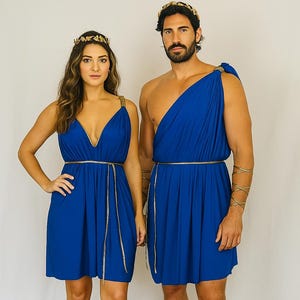 May include: Two people in matching royal blue Greek-style costumes. The woman wears a short dress with a plunging neckline, gold belt, and gold sandals. The man wears a draped tunic, gold armbands, and sandals. Both wear gold headbands.