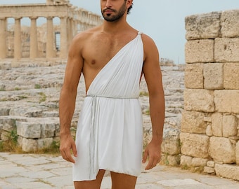 May include: A white one-shoulder tunic featuring a draped design and a thin silver waist tie. The outfit includes a silver leaf-style headpiece and silver leg wraps that extend from the ankles to the calves, paired with dark brown leather sandals.