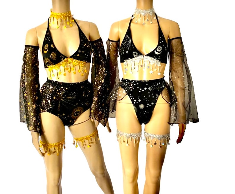 May include: Two matching black and gold celestial-themed lingerie sets. Each set includes a halter top, high-waisted bottoms, arm sleeves, and leg garters. The tops and bottoms are adorned with star and moon patterns, and the sets feature dangling gold or silver accents.