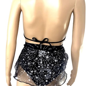 May include: Black halter top, shorts, and garter set. The top ties at the neck and back. The shorts are black with a white star pattern and a sheer overlay. Black star-shaped garter accents complete the set. A celestial-themed outfit.