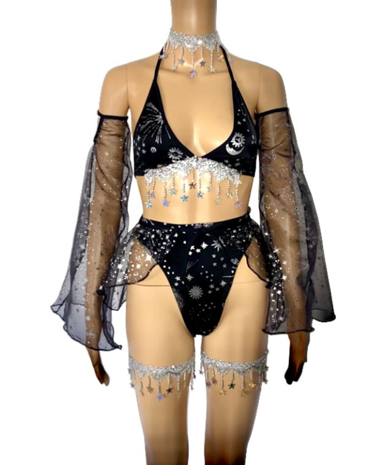 May include: Black lingerie set with a celestial theme. The set includes a halter top, high-waisted bottoms, arm sleeves, a choker, and leg garters. The fabric is adorned with silver stars and celestial patterns, with dangling star accents.
