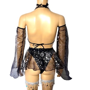 May include: Black lingerie set with a halter top, skirt, and arm sleeves. The set features a celestial design with stars and a sheer skirt. Silver leg chains with star charms complete the look.