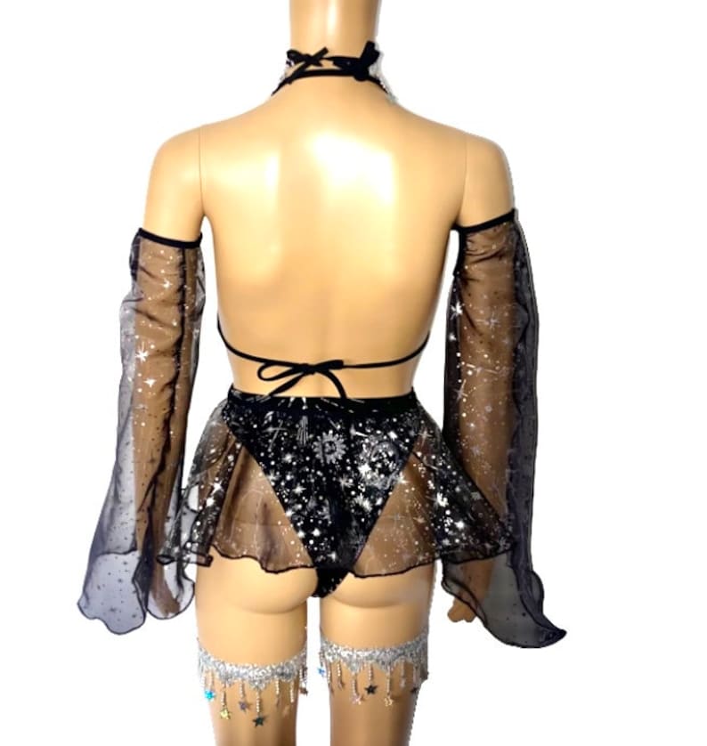 May include: Black lingerie set with a halter top, skirt, and arm sleeves. The set features a celestial design with stars and a sheer skirt. Silver leg chains with star charms complete the look.