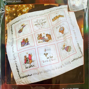 May include: A white stamped lap quilt kit featuring a Christmas nativity scene with the text "Peace on Earth" and "Glory to God in the highest and Peace". The kit includes 45 x 45 inches of fabric, cotton floss, a needle, floss separators, and tri-lingual instructions. Backing and batting are not included. Made in the USA.