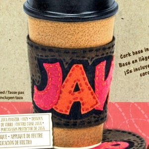 May include: A coffee cup with a black lid and a brown cork sleeve. The sleeve has the word "JAVA" in orange and pink letters. A matching coaster is below the cup. The image also includes text in multiple languages.
