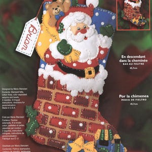 May include: A Bucilla Down the Chimney felt stocking kit featuring a Santa Claus figure, a teddy bear, and a brick chimney design. The kit includes stamped felts, cotton floss, sequins, and beads to create an 18-inch decorative holiday stocking.