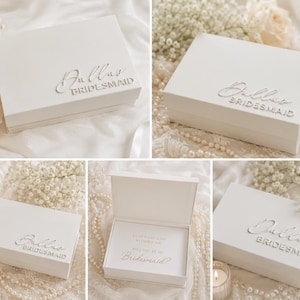 May include: A white rectangular gift box with a hinged lid featuring the name Dallas and the word BRIDESMAID in raised lettering on the top. The interior of the open box displays the text I CAN'T SAY I DO WITHOUT YOU WILL YOU BE MY Bridesmaid?
