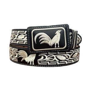May include: A black leather belt featuring a rectangular buckle with an embroidered white rooster design. The belt strap is decorated with a repeating pattern of white embroidered roosters and geometric Greek key border motifs throughout.