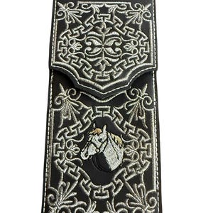 May include: Black leather wallet with intricate white embroidered patterns and a horse head design. The wallet features a flap closure and white stitching along the edges. A stylish accessory for carrying cards and cash.