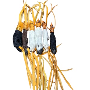 May include: A collection of six animal paw charms with leather straps. The paws vary in color, including black, brown, and white, and are adorned with decorative caps. The leather straps are a light yellow color.
