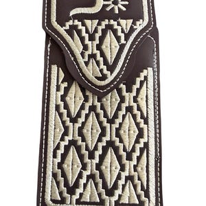 May include: Dark brown leather phone case with intricate cream-colored embroidery. The design features geometric patterns and a stylized floral element on the flap. White stitching outlines the edges, enhancing the detailed craftsmanship.