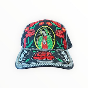 May include: Black trucker hat with embroidered design. Features a central oval with a religious figure, surrounded by a gold halo. Red roses and green leaves are embroidered around the crown and brim. The brim has a large red rose.
