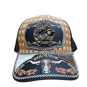 Peut inclure: Casquette de camionneur avec un motif tissé marron et beige sur la couronne et un dos en filet noir. L'avant présente un patch en cuir noir avec le mot "RODEO" et un cow-boy. La visière a un motif de taureau.