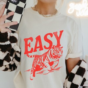 May include: A white t-shirt with a red tiger graphic and the word "EASY" printed in red letters.