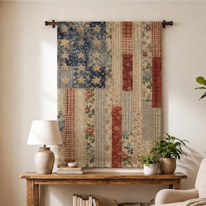 May include: A rectangular wall hanging featuring a patchwork design of the American flag, constructed from various fabric strips with floral, plaid, and striped patterns in muted red, white, and blue tones, suspended from a dark wooden rod.