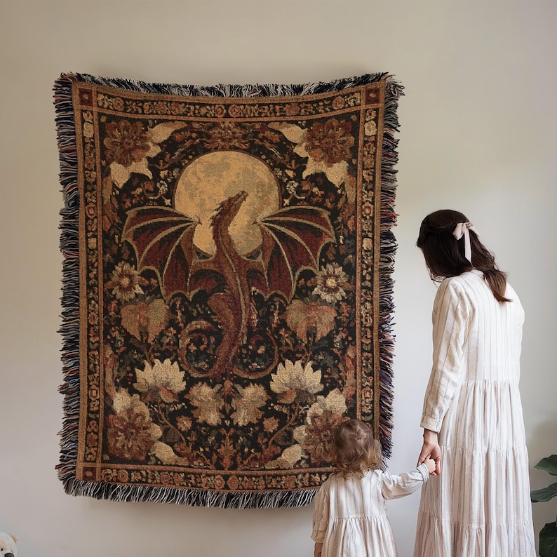 May include: A tapestry featuring a dragon with outstretched wings against a full moon. The tapestry has a dark background with floral and decorative elements in shades of brown, beige, and burgundy. The edges are fringed.