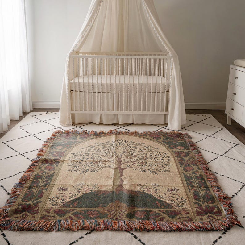 Peut inclure: Une couverture tiss&eacute;e avec un motif d'arbre, fond beige, colline verte et bordure d&eacute;corative. Le plaid est pos&eacute; sur un tapis blanc devant un lit b&eacute;b&eacute; blanc.