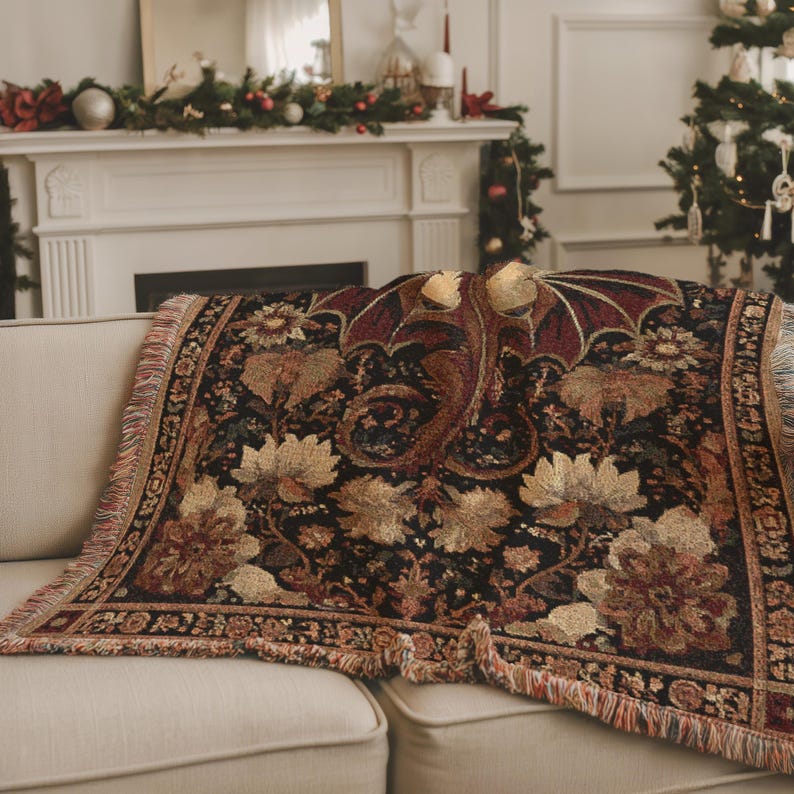 May include: A decorative throw blanket featuring a dragon design with a black background and floral accents. The blanket has a fringed edge and is draped over a beige sofa. The dragon is in shades of red and gold.