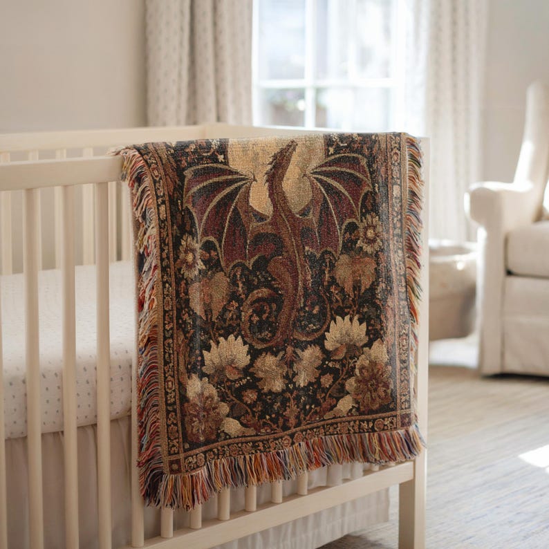May include: A tapestry throw blanket with a dragon design draped over a white crib. The blanket features a dragon with outstretched wings in shades of brown and red, set against a dark floral background. The edges have a fringed trim.