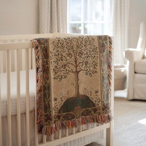 Peut inclure: Une couverture en tapisserie tiss&eacute;e avec un motif d'arbre drap&eacute;e sur un berceau blanc. La couverture pr&eacute;sente un motif d'arbre central en marron et vert, avec un fond beige et une frange color&eacute;e.