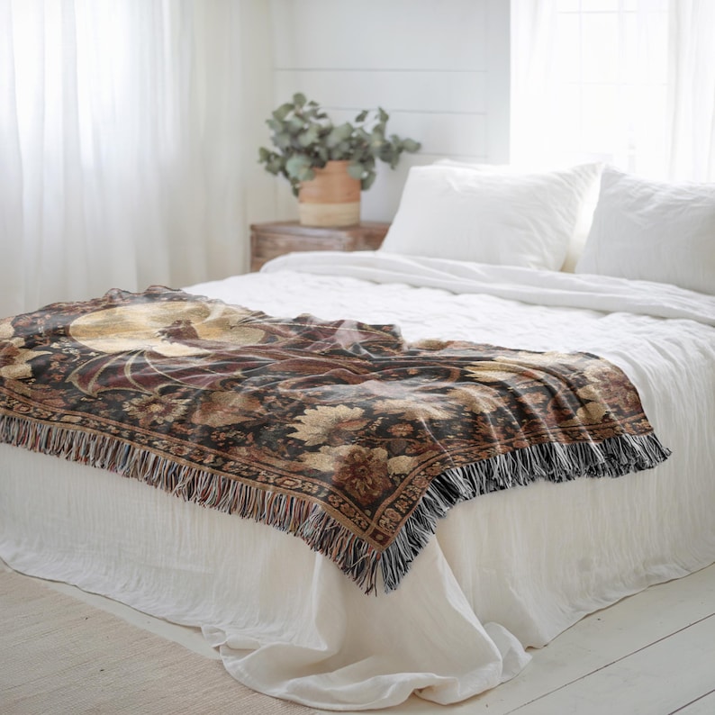 May include: A decorative throw blanket with a floral design in shades of brown, gold, and burgundy, fringed edges, draped over a white bed. The blanket features a detailed pattern and adds a touch of elegance to the bedroom decor.