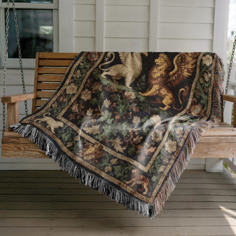 May include: A woven tapestry throw blanket featuring a griffin and lion design in shades of gold, tan, and brown on a black background. The blanket has a fringed edge and is draped over a wooden swing.