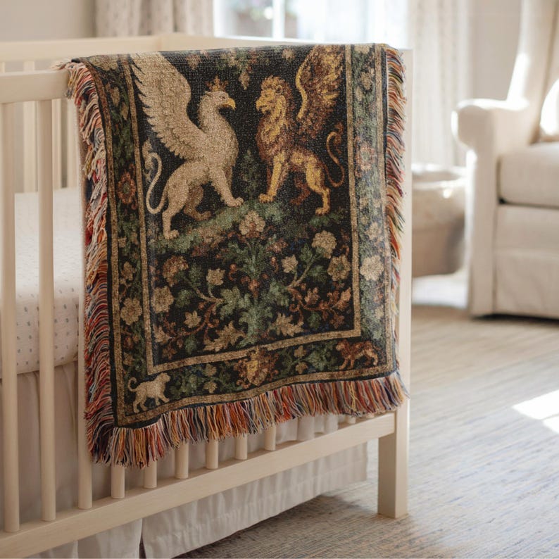 May include: A woven tapestry blanket draped over a white crib. The blanket features a design of a griffin and a winged lion, with floral and foliage details in shades of green, brown, and gold. The blanket has a fringed edge.