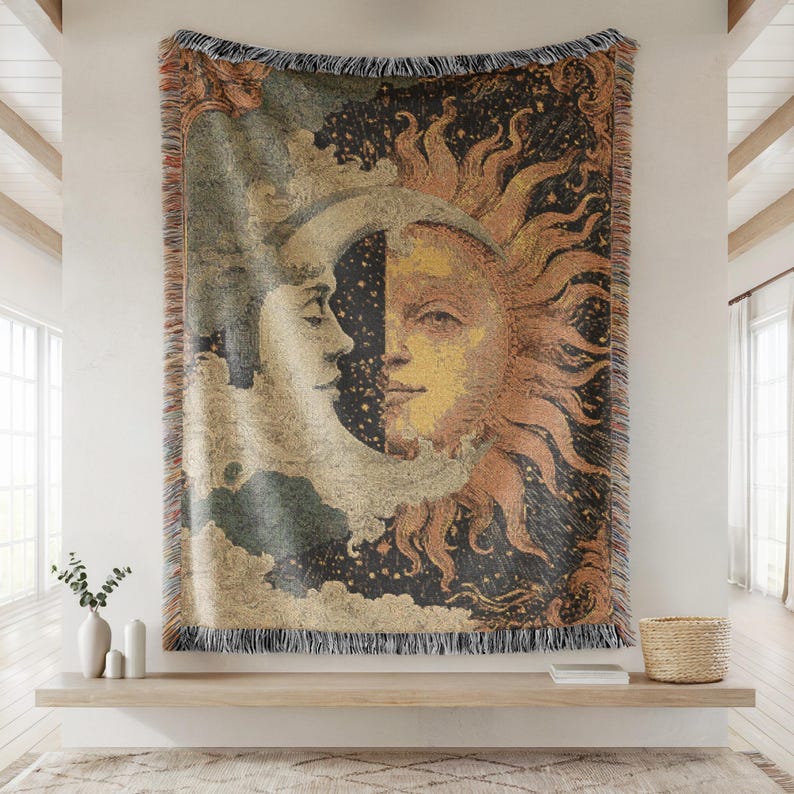 May include: Woven tapestry featuring a celestial design with the sun and moon. The artwork depicts the sun in shades of orange and yellow, and the moon in cream and gray, set against a dark starry background. The tapestry has a fringed edge.