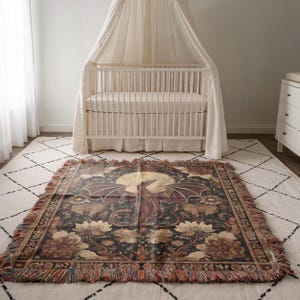 May include: A woven throw blanket featuring a dragon design with a full moon in the background. The blanket has a black background with floral and foliage patterns in shades of brown, gold, and red. The blanket is rectangular with fringed edges.