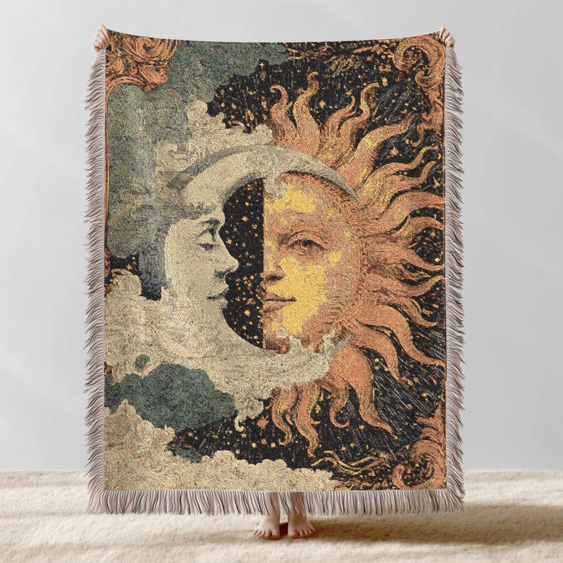May include: Woven throw blanket featuring a celestial design with the sun and moon. The artwork depicts the sun and moon facing each other, with a starry night sky background. The blanket has a fringed edge and is in shades of beige, gold, and black.