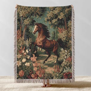 May include: A woven throw blanket featuring a brown horse rearing up in a forest scene. The tapestry-style design includes trees, flowers, and a path, with a fringed edge. The color palette includes shades of brown, green, and red.
