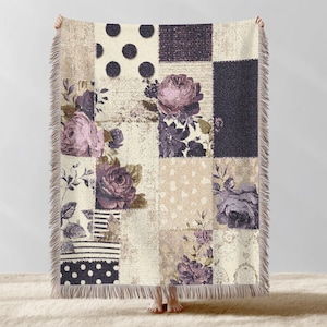 May include: A patchwork throw blanket with a floral design. The blanket features squares with polka dots, floral patterns, and solid colors in shades of beige, purple, and black. The edges have a fringed trim.