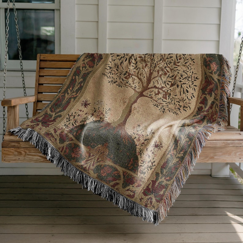 Peut inclure: Une couverture tiss&eacute;e avec un motif d'arbre drap&eacute;e sur une balan&ccedil;oire de porche en bois. La couverture pr&eacute;sente un fond beige avec une illustration d&eacute;taill&eacute;e d'arbre en marron et vert, encadr&eacute;e par une bordure d&eacute;corative avec des franges.