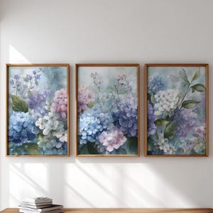 May include: Three framed floral art prints featuring watercolor paintings of hydrangeas in shades of blue, purple, pink, and white. The artwork is set against a soft, light blue background, with wooden frames. The overall theme is botanical and decorative.