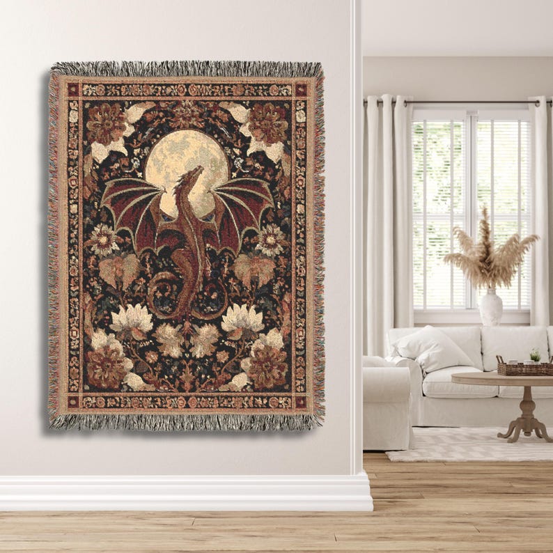 May include: Woven tapestry throw blanket featuring a dragon with outstretched wings in front of a full moon. The dragon is brown and red, set against a dark background with floral and botanical elements. The blanket has a fringed edge.