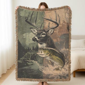 May include: Woven throw blanket featuring a deer and a largemouth bass leaping from water. The design has a vintage aesthetic with a color palette of greens, browns, and tans. The blanket has fringed edges and is held up by a person.