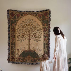 Peut inclure: Une tapisserie avec un motif d'arbre d&eacute;taill&eacute; sur fond beige, encadr&eacute;e d'une bordure d&eacute;corative verte et rouge. La tapisserie a une bordure &agrave; franges. Une femme et un enfant se tiennent &agrave; c&ocirc;t&eacute; de la tapisserie.