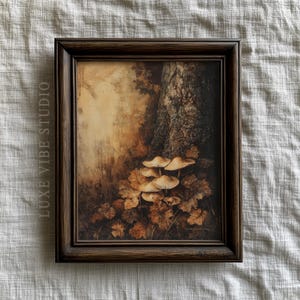 May include: A framed art print featuring a forest scene with mushrooms and fallen leaves in shades of brown and beige. The artwork is set against a neutral background and framed in a dark brown wooden frame. The text "LUXE VIBE STUDIO" is printed on the left side.