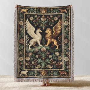 May include: A tapestry throw blanket featuring a griffin and a lion with wings facing each other. The blanket has a dark background with floral and foliage patterns in shades of green, brown, and gold. The edges are fringed.