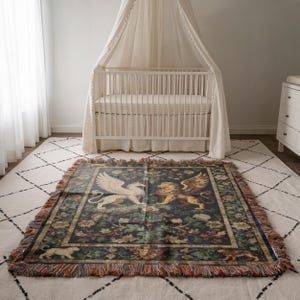 May include: A rectangular tapestry throw blanket with a dark background and a detailed design featuring a griffin and a lion. The blanket has a fringed edge with multiple colors and is placed on a white rug.