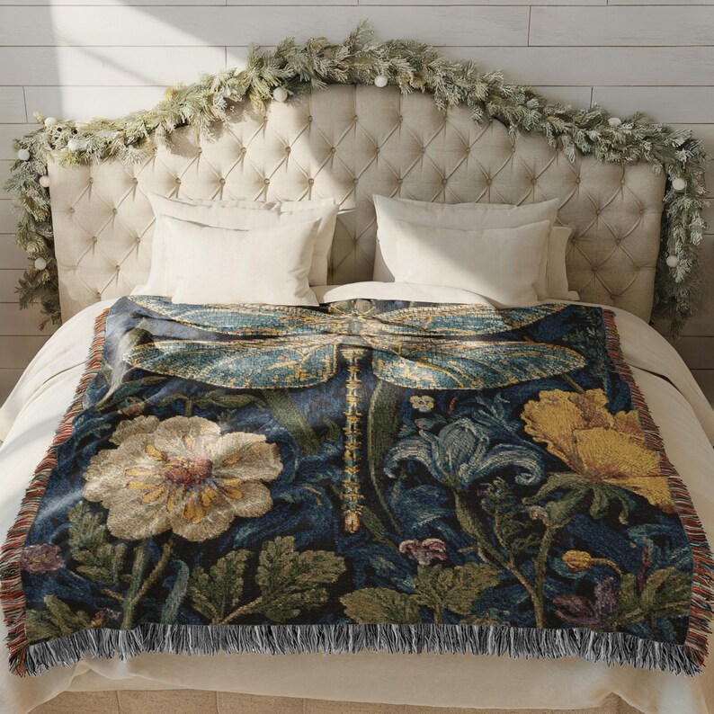 Puede incluir: Una manta decorativa con un dise&ntilde;o de lib&eacute;lula, con un fondo azul oscuro y elementos florales y bot&aacute;nicos en tonos de amarillo, verde y crema. La manta tiene un borde con flecos y se muestra en una cama.