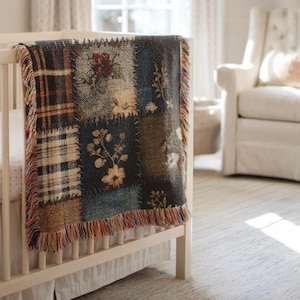 May include: A patchwork baby blanket with floral and plaid patterns in shades of blue, brown, and beige. The blanket has a fringed edge and is draped over a white cot.
