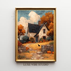 May include: A framed painting of a quaint cottage scene in autumn. The artwork features a stone cottage with a dark roof, surrounded by orange trees and pumpkins. A black cat sits on the path. The frame is gold, and the text "LUXE VIBE STUDIO" is at the bottom.