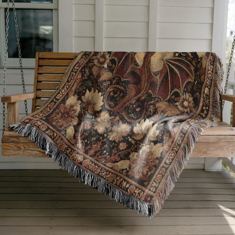 May include: A woven throw blanket with a dragon and floral design in shades of brown, black, and tan. The blanket is draped over a wooden porch swing and has a fringed edge.